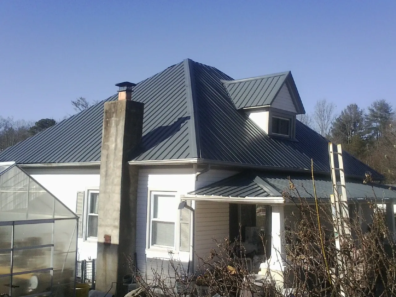 Dark blue standing seam metal roof on a white farmhouse with dormer — Slate & Tile Roof Repair by Roofing Brothers in Luverne